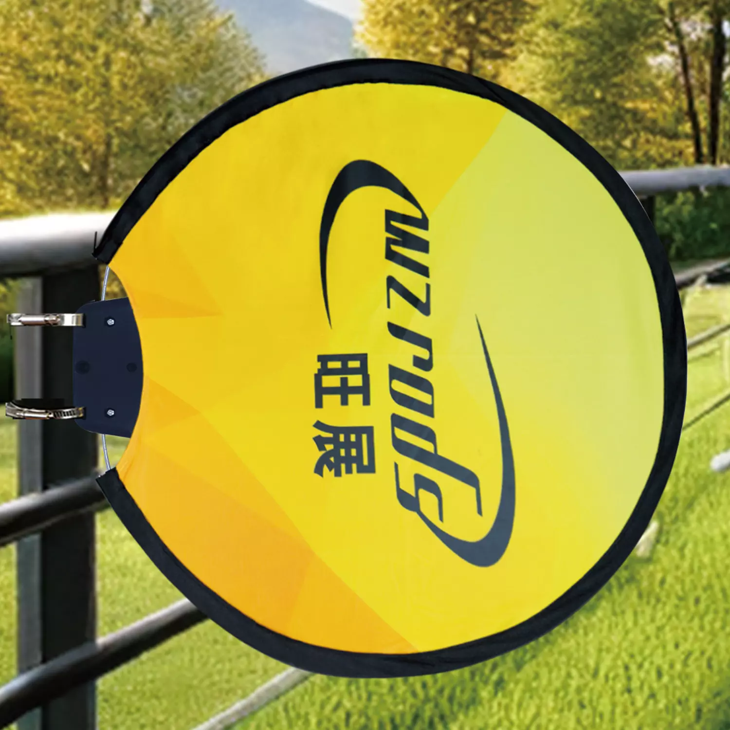Yellow circular 旺展 Sun banner secured to a railing with cable ties. Outdoor setting with green grass, designed for light pole or fence mounting at events.