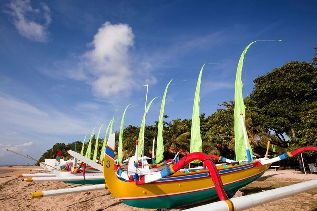 Traditional boats with green sails and Bali-style flags at beach Traditional boats with tall sails and Bali-style flags at serene beach harbor.