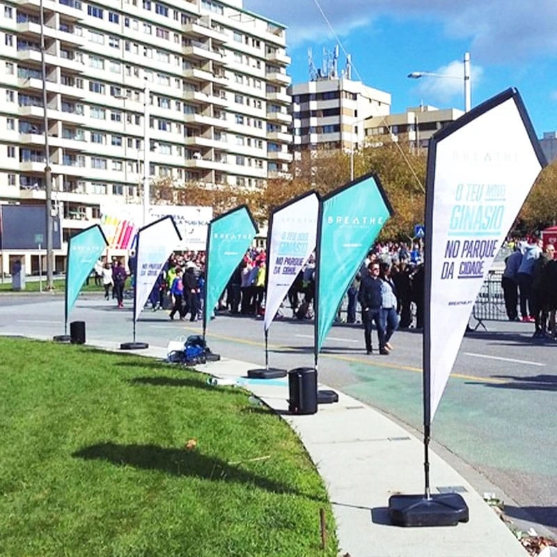Four athletes demonstrating K banner deployment in park settings: white/teal fabric panels with water tank. Visible water tank base plates ensure stability on stone pavement during fitness events.