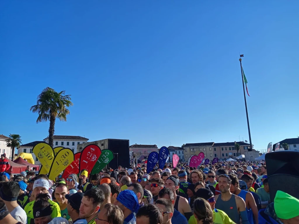 Gruppo di corridori con bandierine multicolore di ritmo, tra cui diversi con zaini WZRODS per pacemaker di maratona
