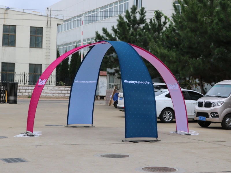 Pink and blue double-sided arch banner stand with text 'displays people' in outdoor parking lot