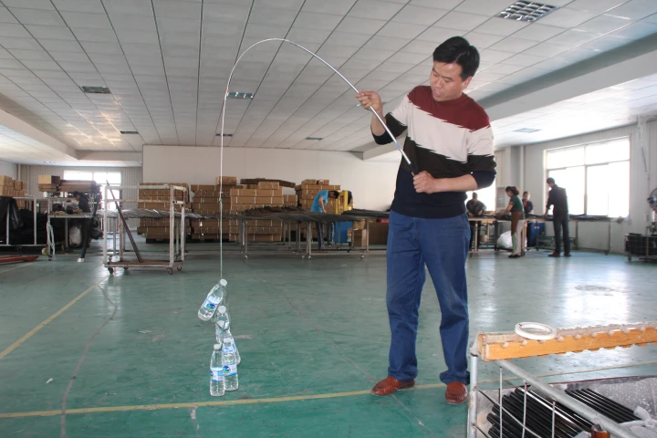 A man testing the load-bearing capacity of a carbon fiber flagpole by horizontally suspending multiple water bottles in a factory setting.