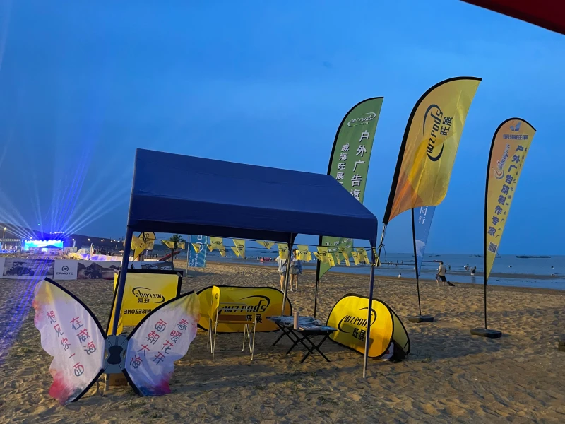 Beach event setup with feather flags, teardrop flags, pop-up banner and cafe barrier at twilight