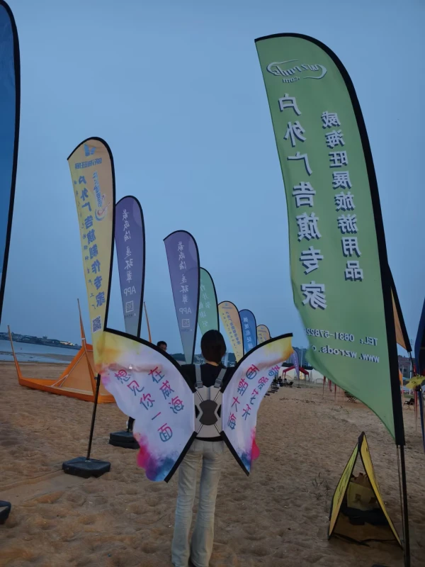 Person wearing backpack banner M with feather flags on sandy beach