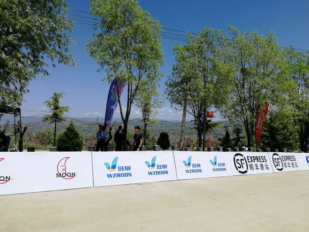 Outdoor event with sideline banners (WZRODS, SF Express, MOON) against a scenic backdrop, trees, and distant hills.