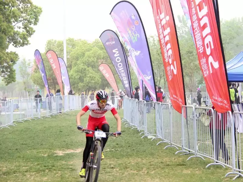 Cycling race, red/white athlete, and WOOM sponsorship flags at outdoor track.