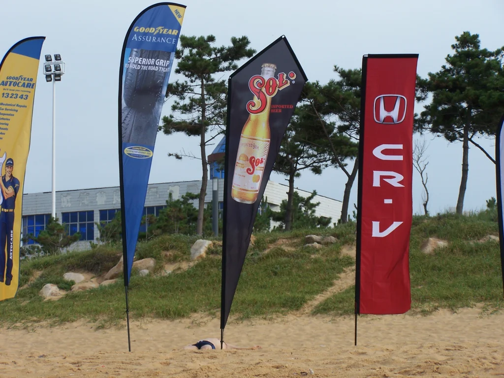 Coastal marketing teardrop flags for GOODYEAR tires and Sol beer near sandy shore