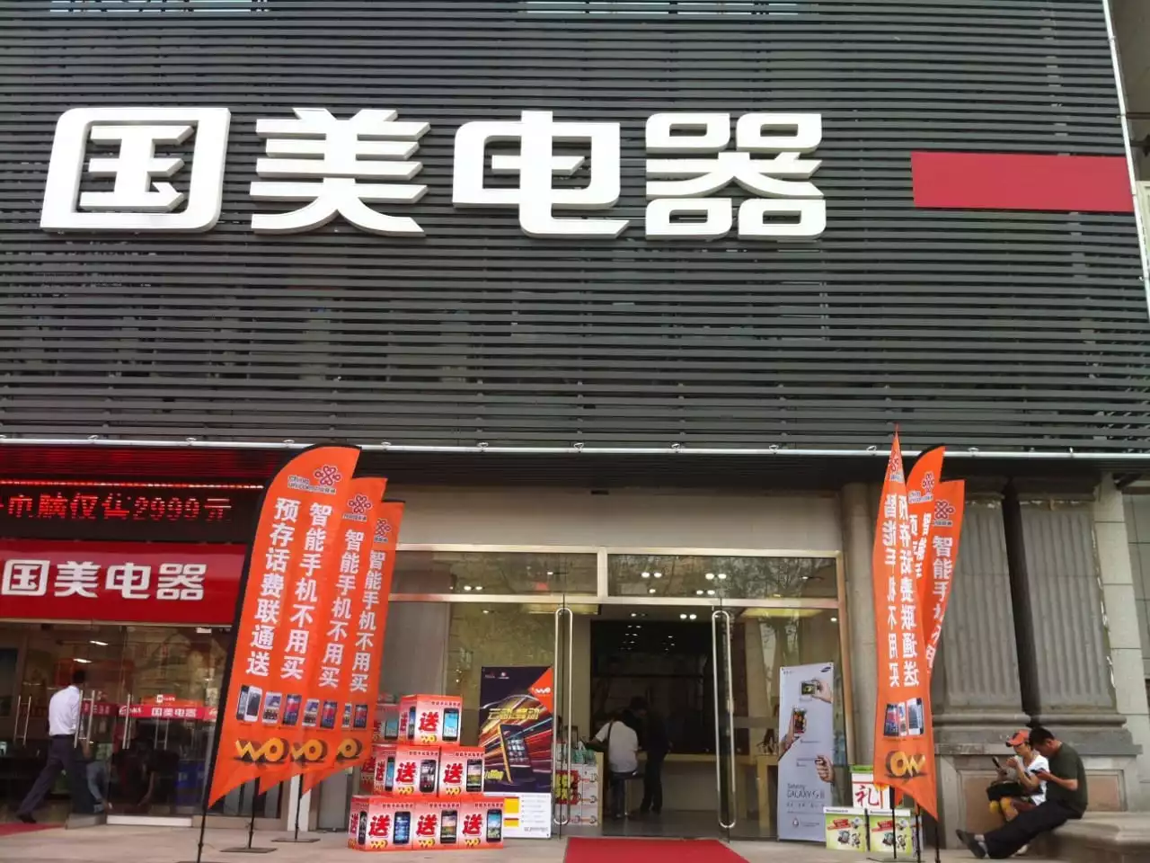 Orange bowhead flags displaying phone promotions at busy electronics store entrance with red product displays