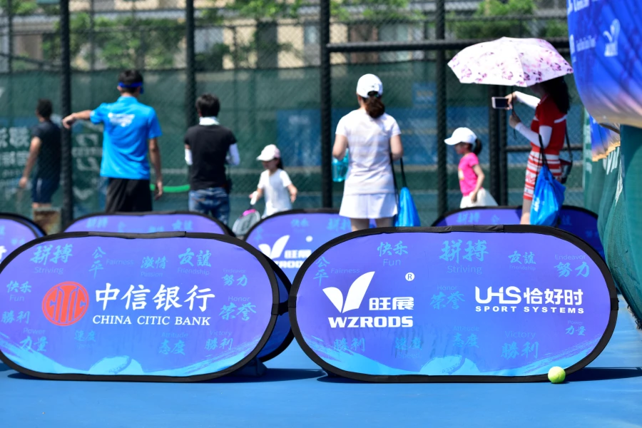 Blue sideline banners (China Citic Bank, WZRODS) on tennis court, people (adults, kids) in background, event setup.