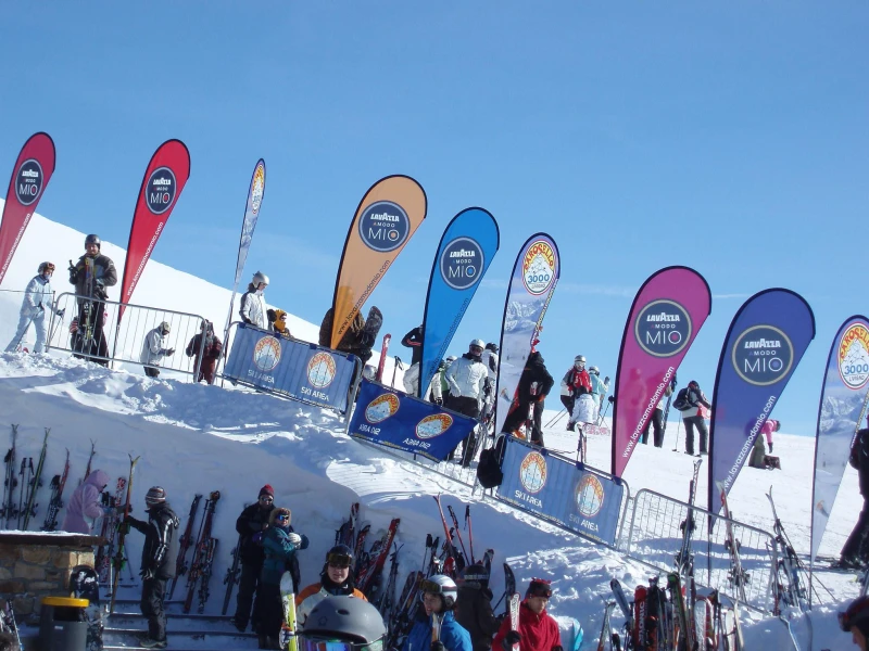 Colorful LAVAZZA MIO teardrop flags marking ski slope with active winter sports participants