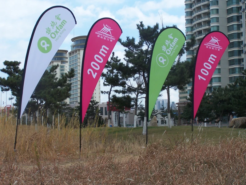 Oxfam Trailwalker charity walk distance marker flags (200m, 100m) on a field with city skyline.