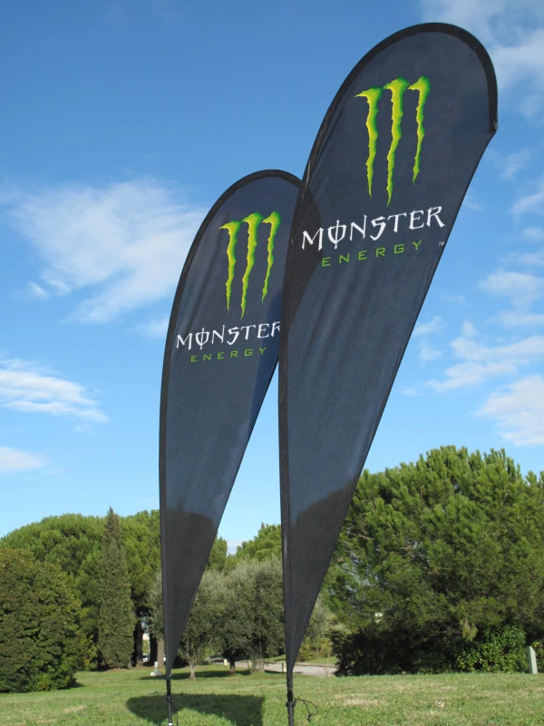 Black MONSTER ENERGY teardrop flags with green claw marks on grassy outdoor field
