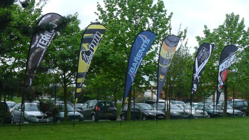 Six consecutive teardrop flags lining grassy parking lot area