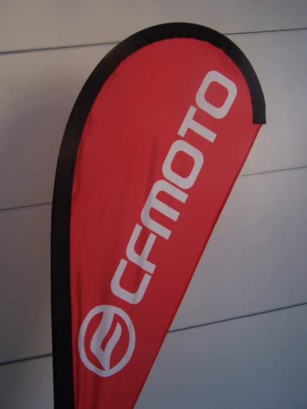 Red CFMOTO teardrop banner with white logo on black outline against industrial background