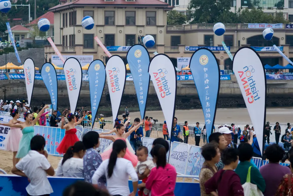 Double-sided custom flags at a beach event with dancers and crowd, showing clear branding from all angles.